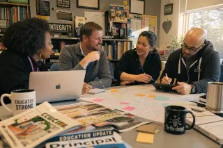Teachers in a lounge collaborating closely on lesson plans, surrounded by resources and warm natural light, in an authentic moment of professional exchange.