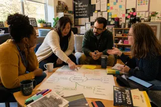Four teachers in a cozy lounge discussing a colorful mind map on Bloom's taxonomy, surrounded by notes and resources, in a natural and collaborative setting.