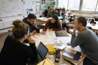 Secondary teachers in deep collaborative discussion around a messy classroom table, brainstorming project ideas with visible notes and gentle natural lighting.