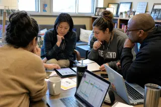 Teachers in a lounge collaborating over digital devices and notes in a natural, warm atmosphere