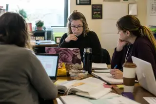Teachers collaborating around a table in a lively teachers' lounge, working together on quiz design in a natural, documentary style.