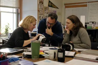 Three teachers in a real staff room, collaborating around VR headsets and lesson plans in a warm, sunlit atmosphere.