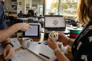 Teachers in a staff room reviewing a 3D-printed object together, surrounded by project materials and natural afternoon light.