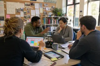 Teachers collaborating around a table in a real staff room, using laptops and tablets in warm natural light, engaged in reflective teamwork.